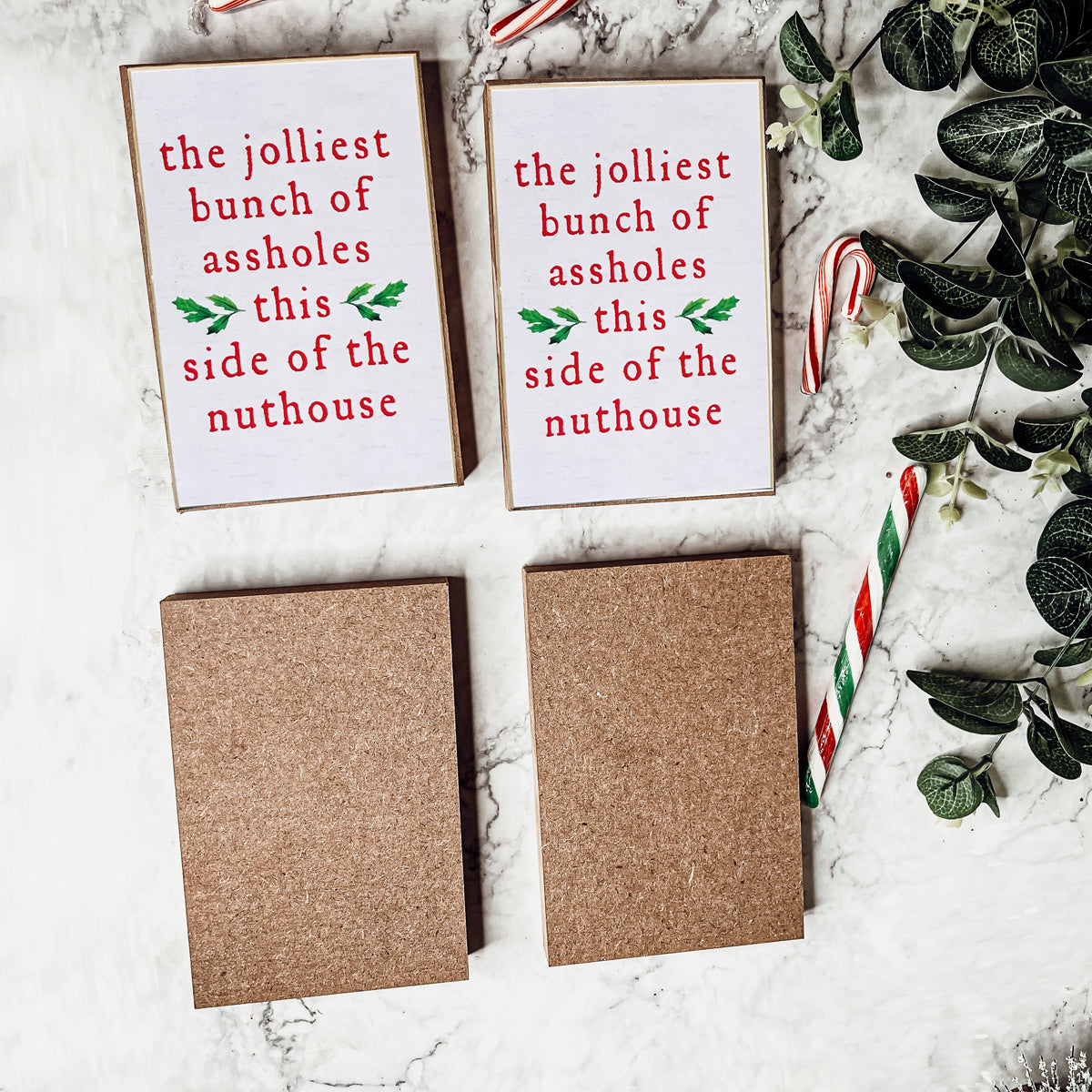 A humorous Christmas sign reading 'The jolliest bunch of assholes this side of the nuthouse', perfect for holiday decor.
