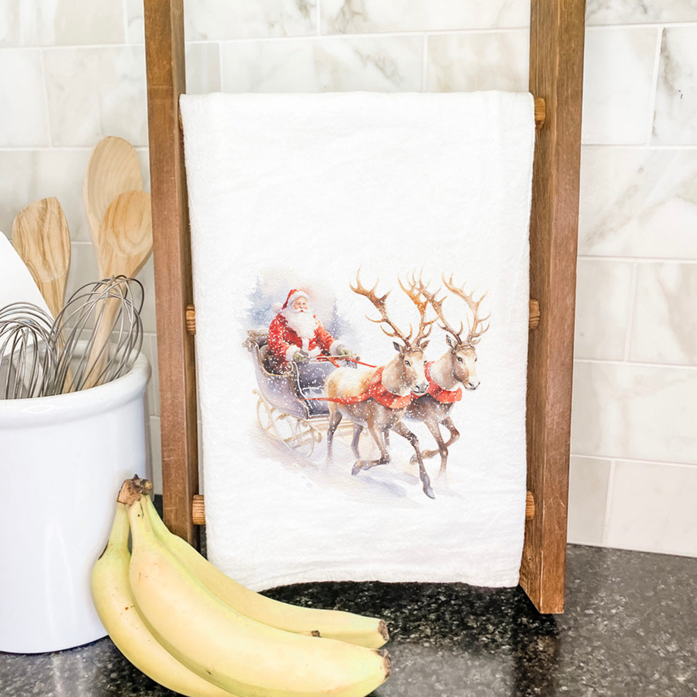 A festive cotton tea towel featuring a colorful Santa and reindeer sleigh design, perfect for holiday kitchen decor.