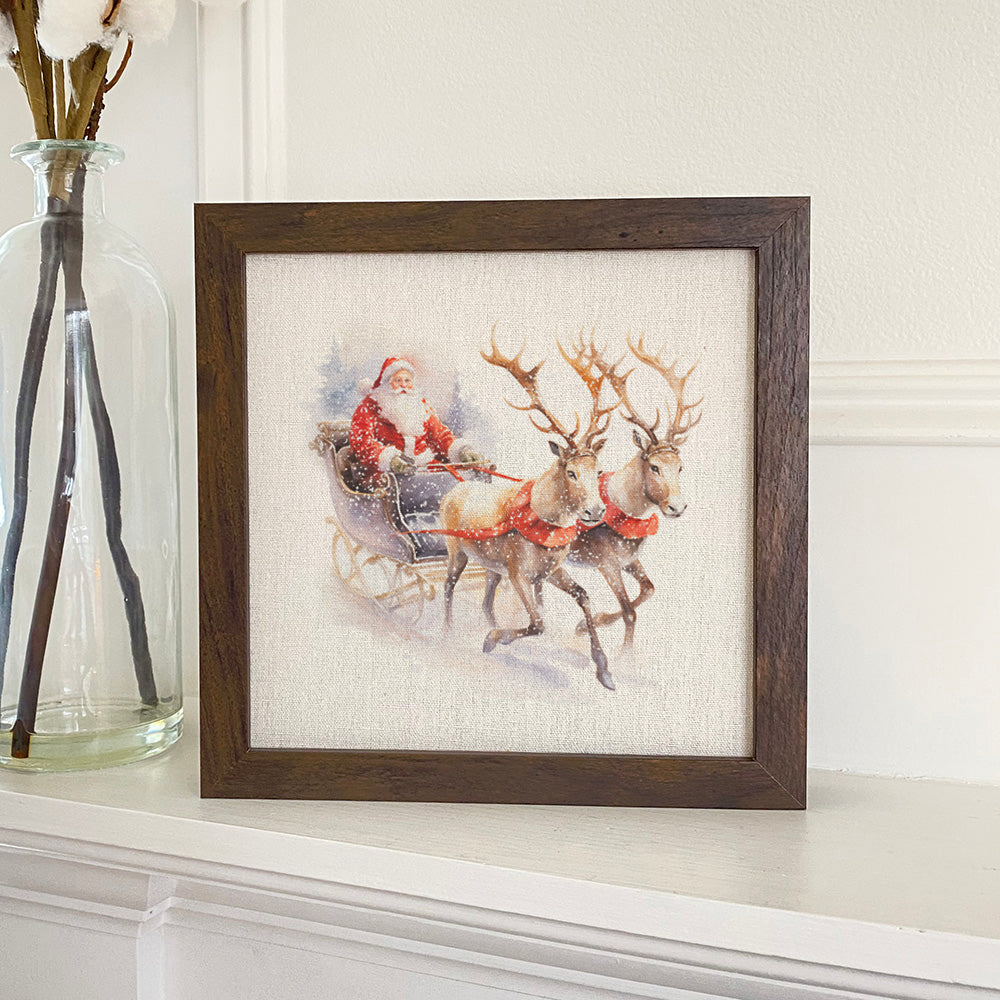 A beautifully framed sign featuring Santa and a reindeer sleigh, set against a linen-look background, available in walnut or white-washed frame.