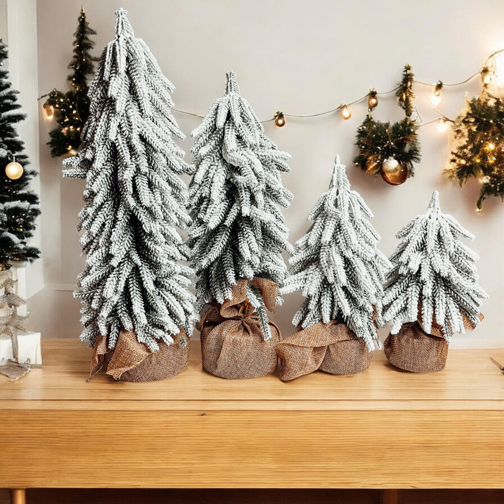 A set of four snow-covered Christmas trees in varying sizes, featuring a jute-covered wooden base, perfect for holiday decor.