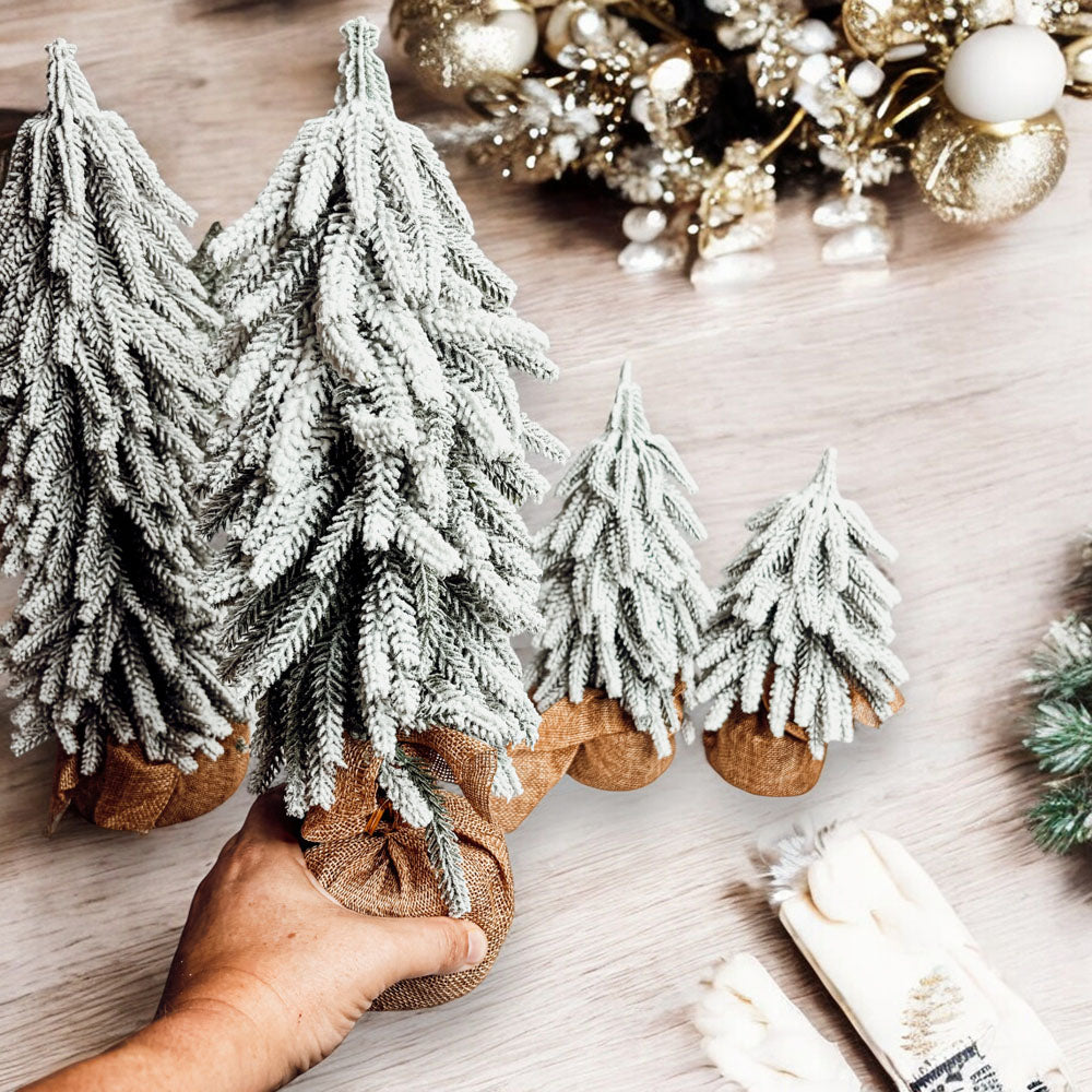 A set of four snow-covered Christmas trees in varying sizes, featuring a jute-covered wooden base, perfect for holiday decor.