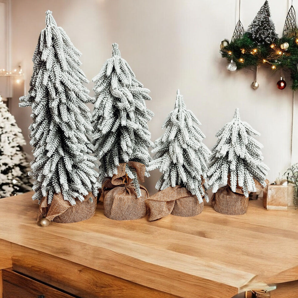 A set of four snow-covered Christmas trees in varying sizes, featuring a jute-covered wooden base, perfect for holiday decor.