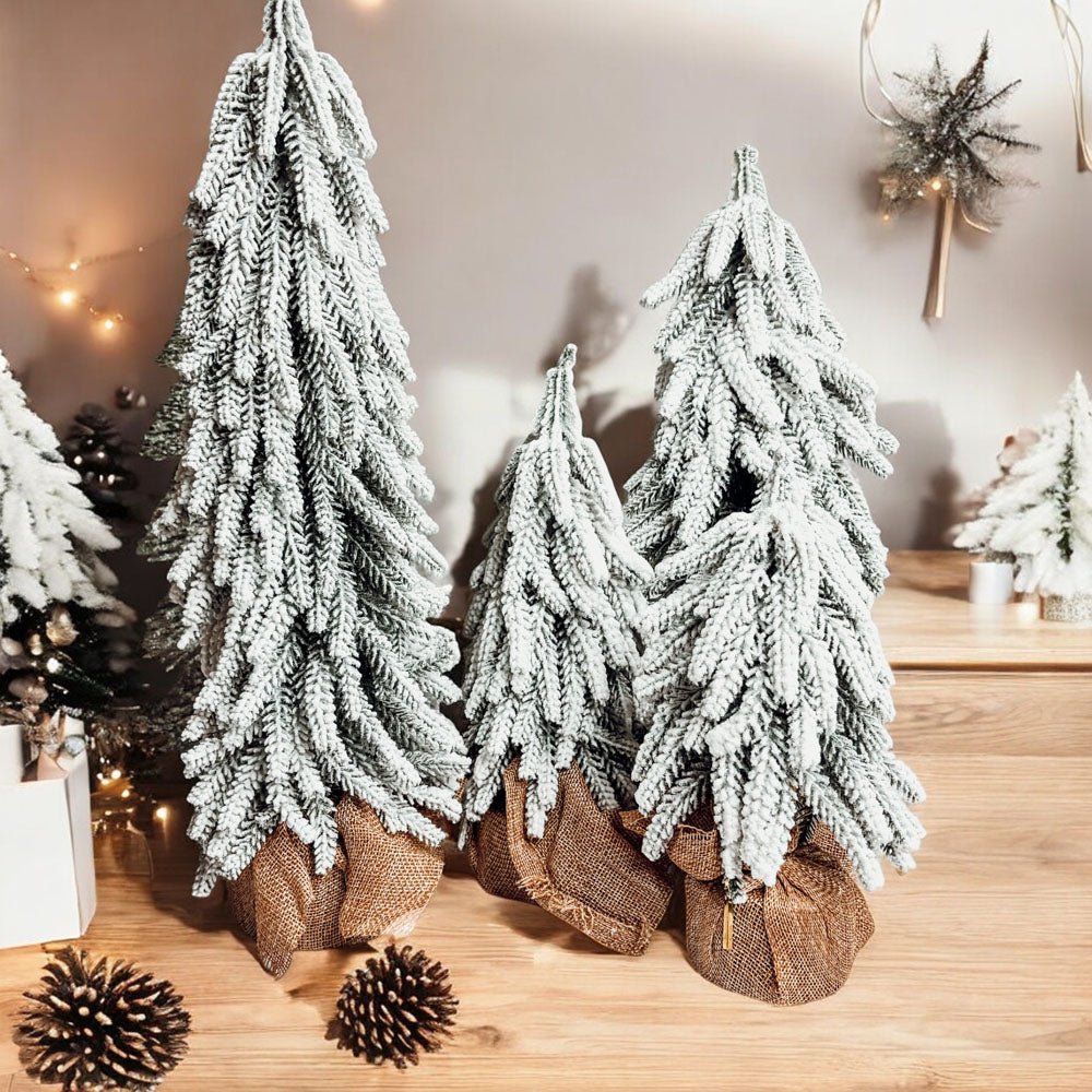 A set of four snow-covered Christmas trees in varying sizes, featuring a jute-covered wooden base, perfect for holiday decor.