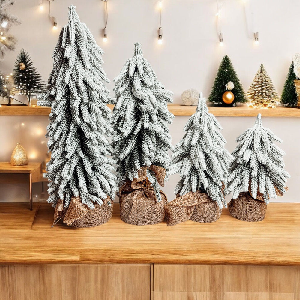 A set of four snow-covered Christmas trees in varying sizes, featuring a jute-covered wooden base, perfect for holiday decor.