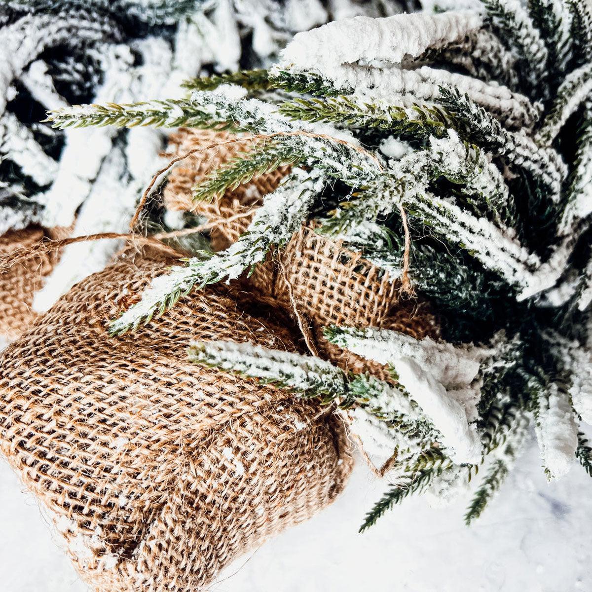 A set of four snow-covered Christmas trees in varying sizes, featuring a jute-covered wooden base, perfect for holiday decor.
