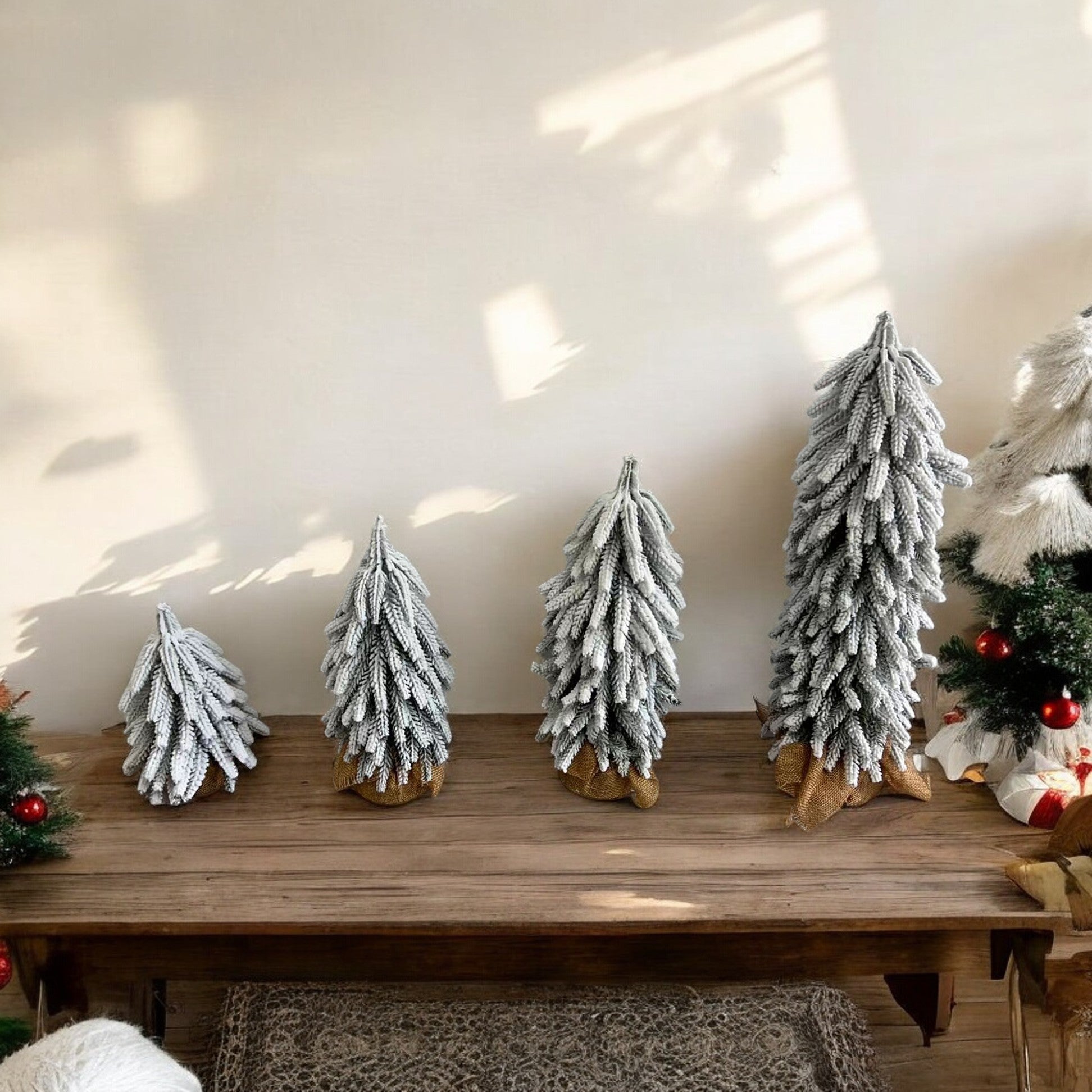 A set of four snow-covered Christmas trees in varying sizes, featuring a jute-covered wooden base, perfect for holiday decor.
