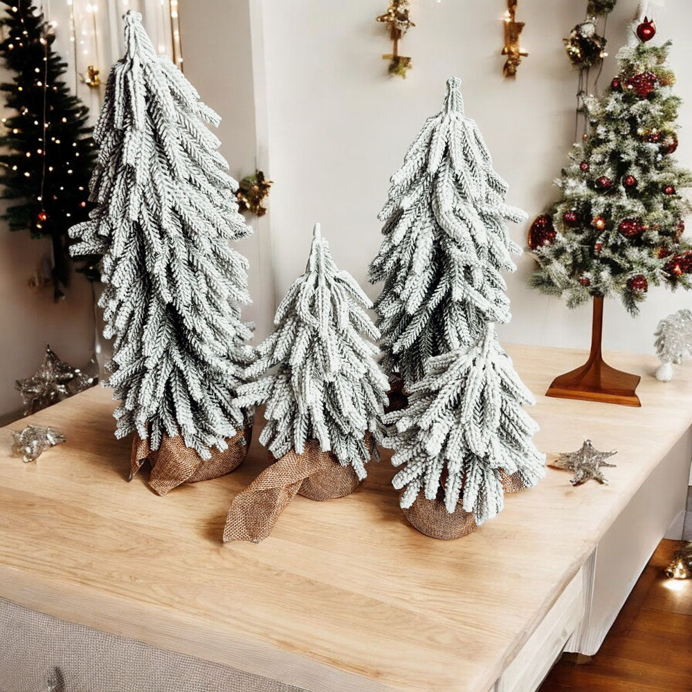 A set of four snow-covered Christmas trees in varying sizes, featuring a jute-covered wooden base, perfect for holiday decor.