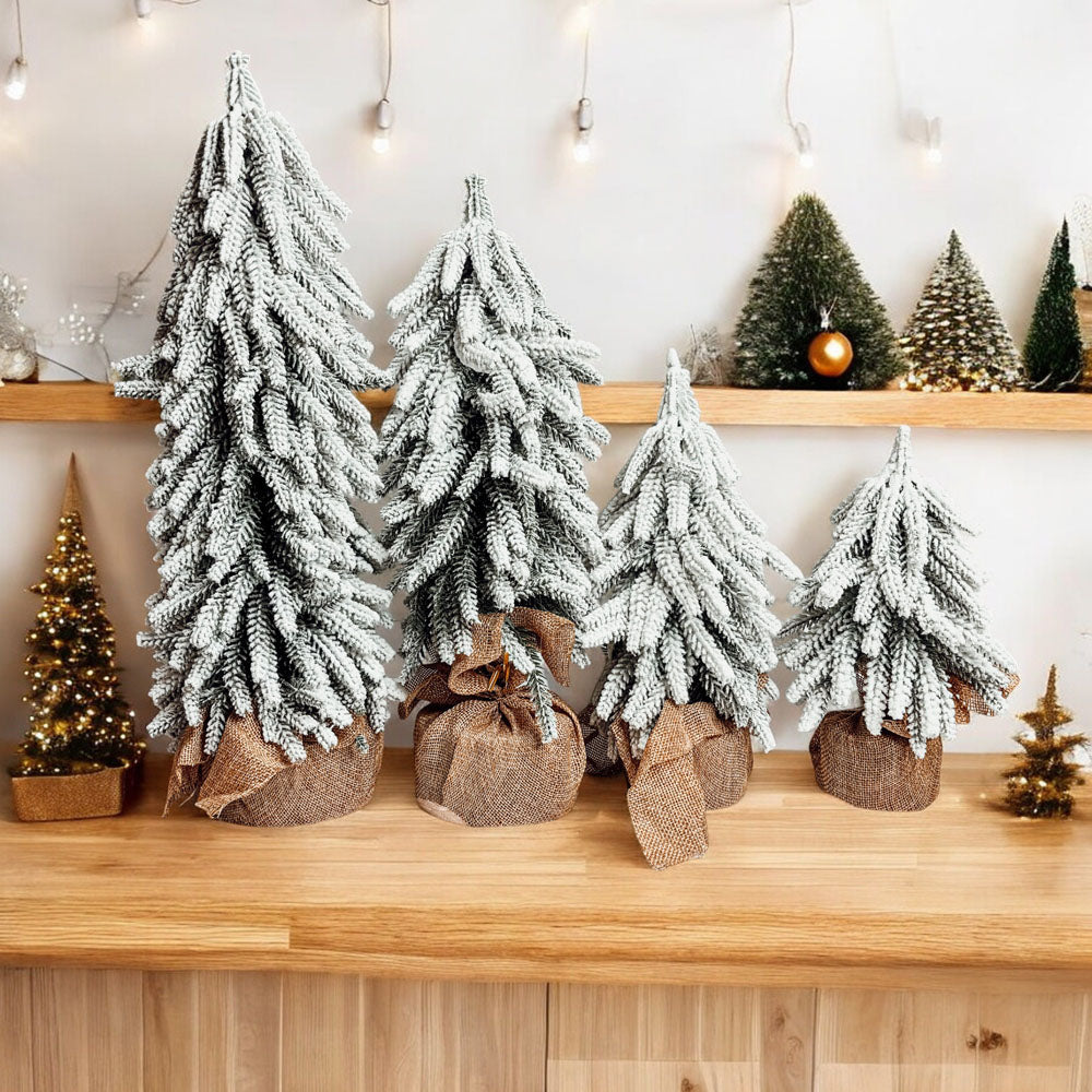 A set of four snow-covered Christmas trees in varying sizes, featuring a jute-covered wooden base, perfect for holiday decor.