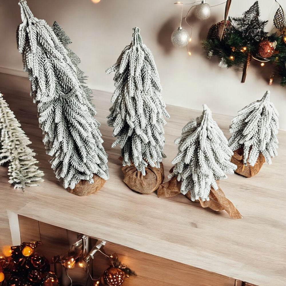 A set of four snow-covered Christmas trees in varying sizes, featuring a jute-covered wooden base, perfect for holiday decor.