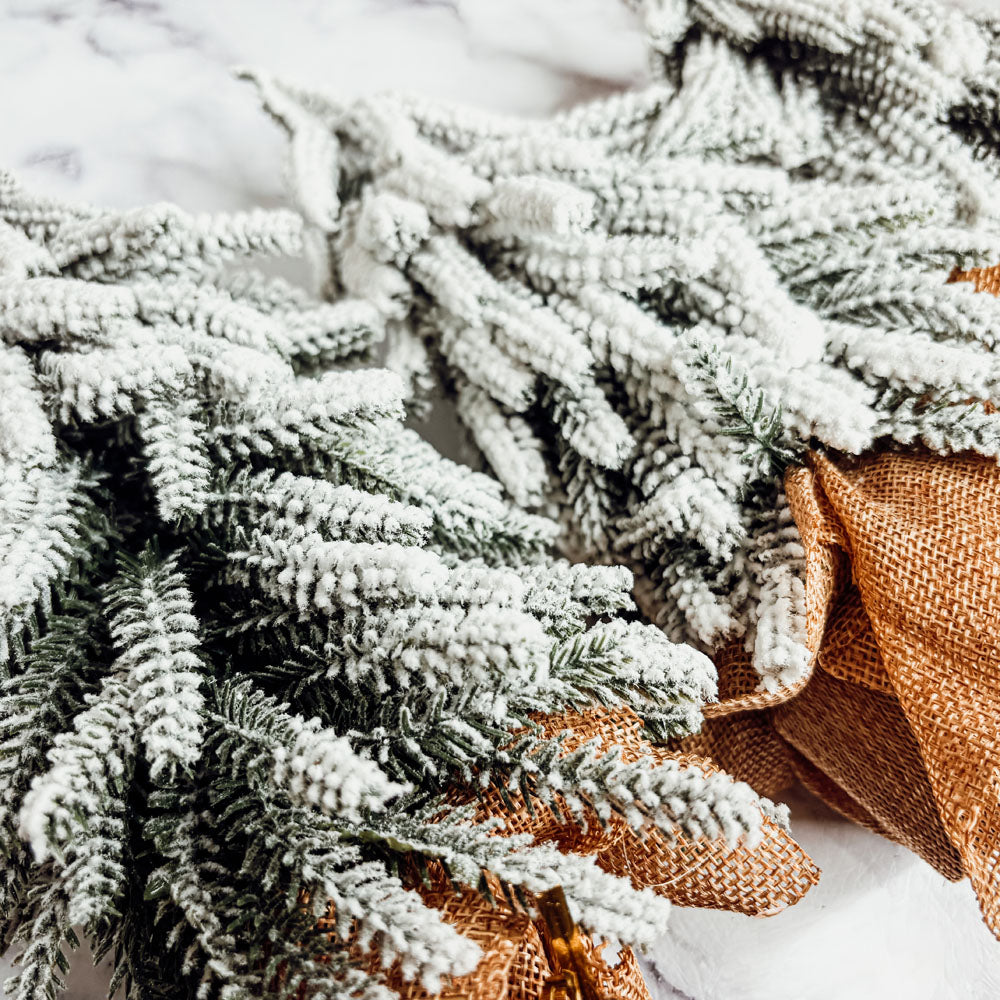 A set of four snow-covered Christmas trees in varying sizes, featuring a jute-covered wooden base, perfect for holiday decor.