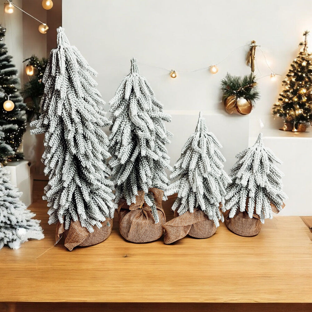 A set of four snow-covered Christmas trees in varying sizes, featuring a jute-covered wooden base, perfect for holiday decor.