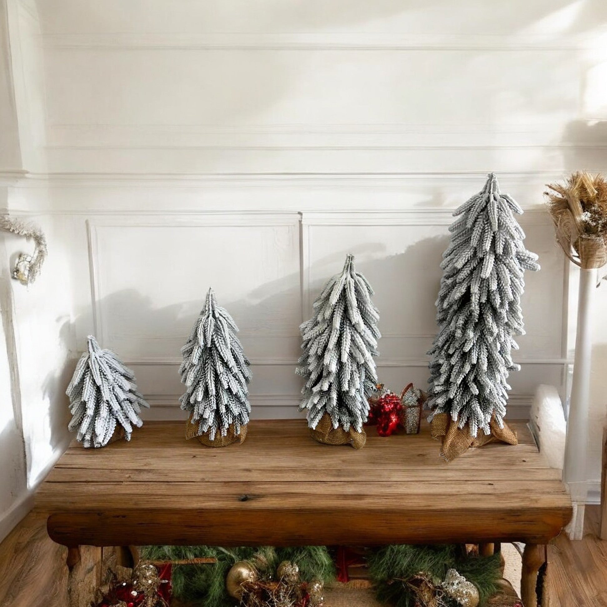 A set of four snow-covered Christmas trees in varying sizes, featuring a jute-covered wooden base, perfect for holiday decor.