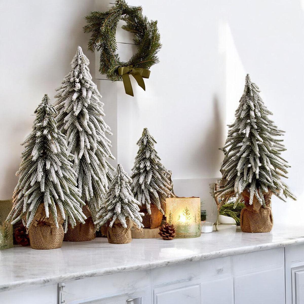 A set of four snow-covered Christmas trees in varying sizes, featuring a jute-covered wooden base, perfect for holiday decor.