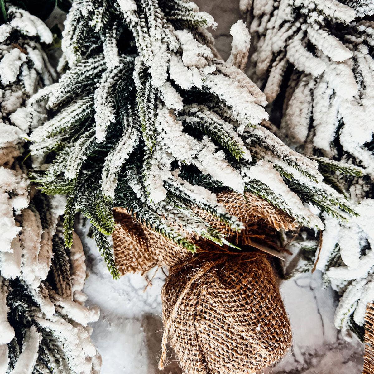 A set of four snow-covered Christmas trees in varying sizes, featuring a jute-covered wooden base, perfect for holiday decor.