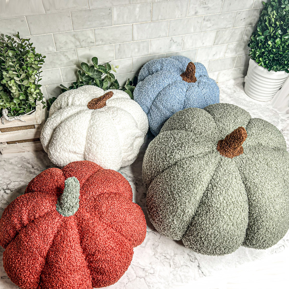 A collection of plush Blair Pumpkins in various colors including blue, gray, and orange, showcasing their soft texture and classic pumpkin shape.