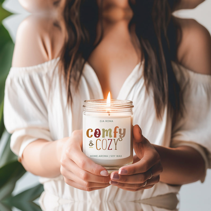 Woman holding lit "Comfy & Cozy" candle.