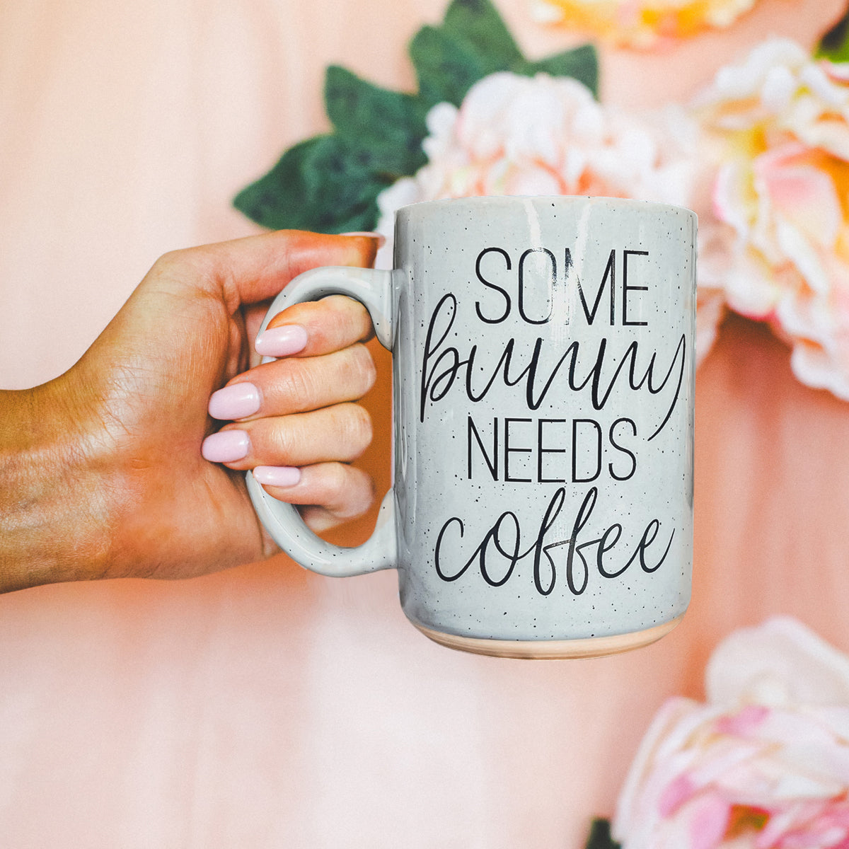Ceramic coffee mug with pastel blue and pink colors, featuring the phrase 'Some Bunny Needs Coffee' on both sides, perfect for Easter and spring.