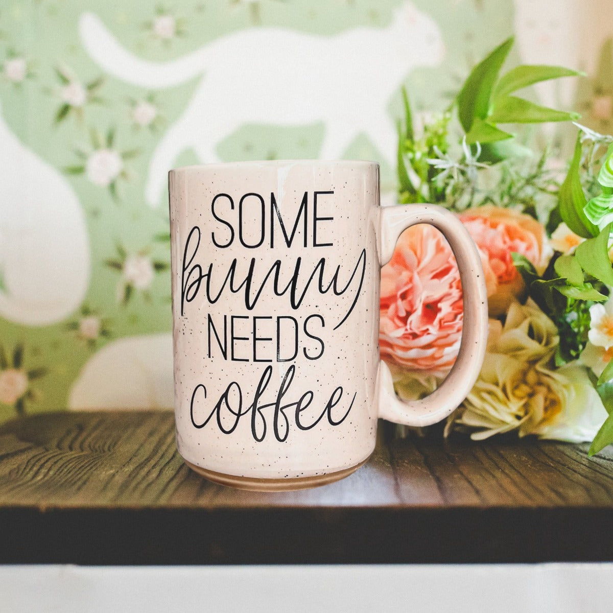 Ceramic coffee mug with pastel blue and pink colors, featuring the phrase 'Some Bunny Needs Coffee' on both sides, perfect for Easter and spring.