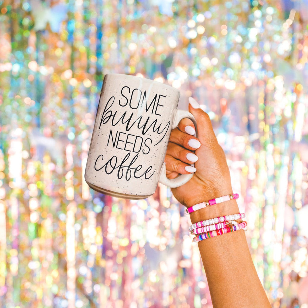 Ceramic coffee mug with pastel blue and pink colors, featuring the phrase 'Some Bunny Needs Coffee' on both sides, perfect for Easter and spring.
