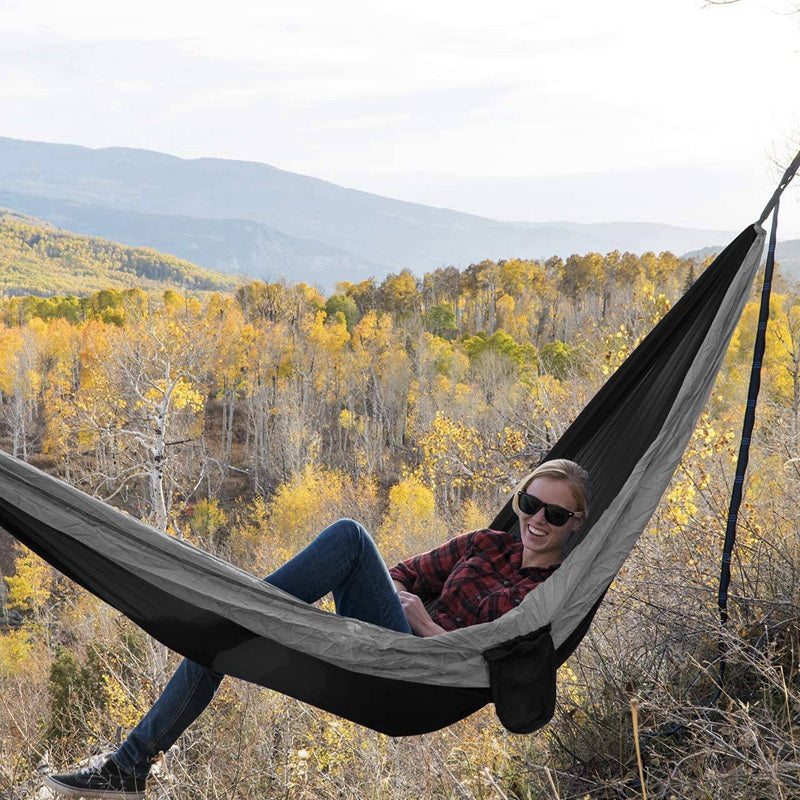 A durable camping parachute hammock set up between two trees, showcasing its spacious design and vibrant color, perfect for outdoor relaxation.