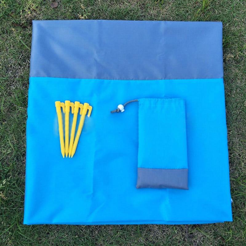 A vibrant waterproof beach blanket in blue and grey, spread out on the sand, showcasing its spacious design and clips for securing it in place.
