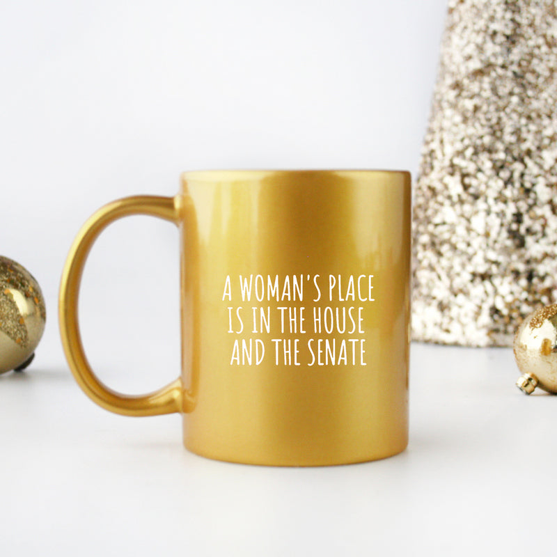A stylish gold and silver ceramic mug with the phrase 'A Woman's Place Is In The House And Senate' elegantly printed on it.