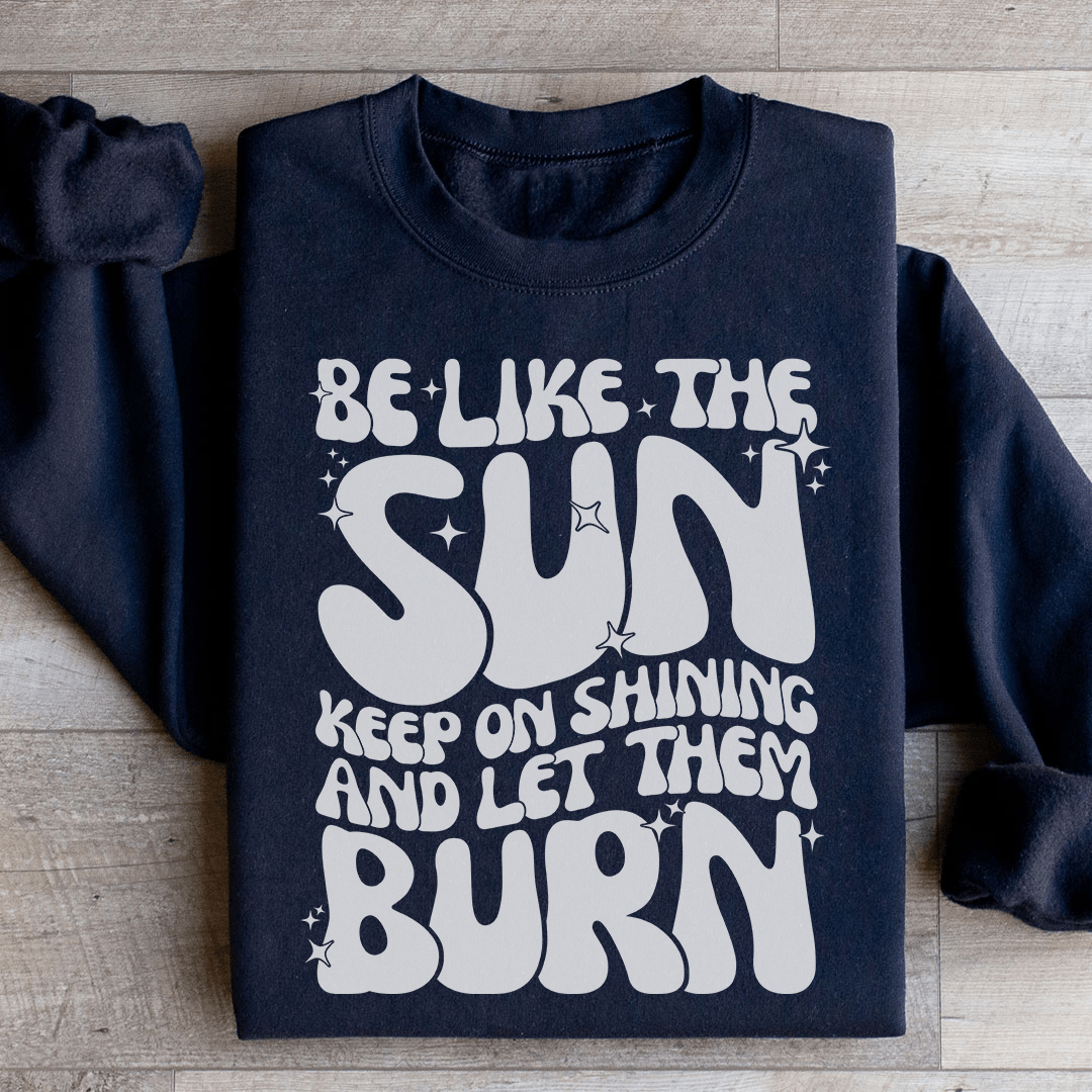 A cozy hoodie featuring the phrase 'Be Like The Sun Keep On Shining And Let Them Burn', designed by top artists, showcasing vibrant colors and a comfortable fit.