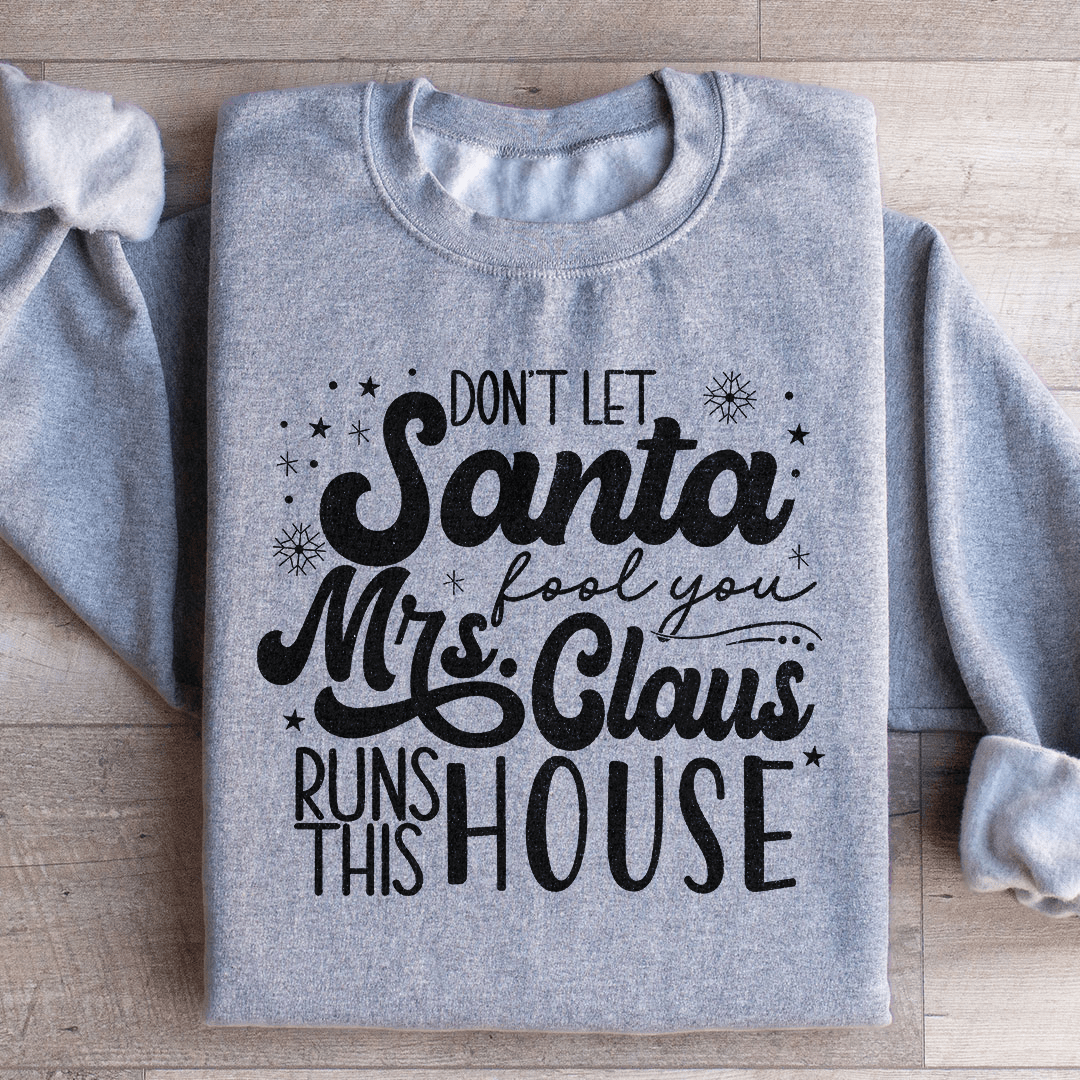 Cozy sweatshirt featuring the phrase 'Don't Let Santa Fool You, Mrs. Claus Runs This House' with a festive design.