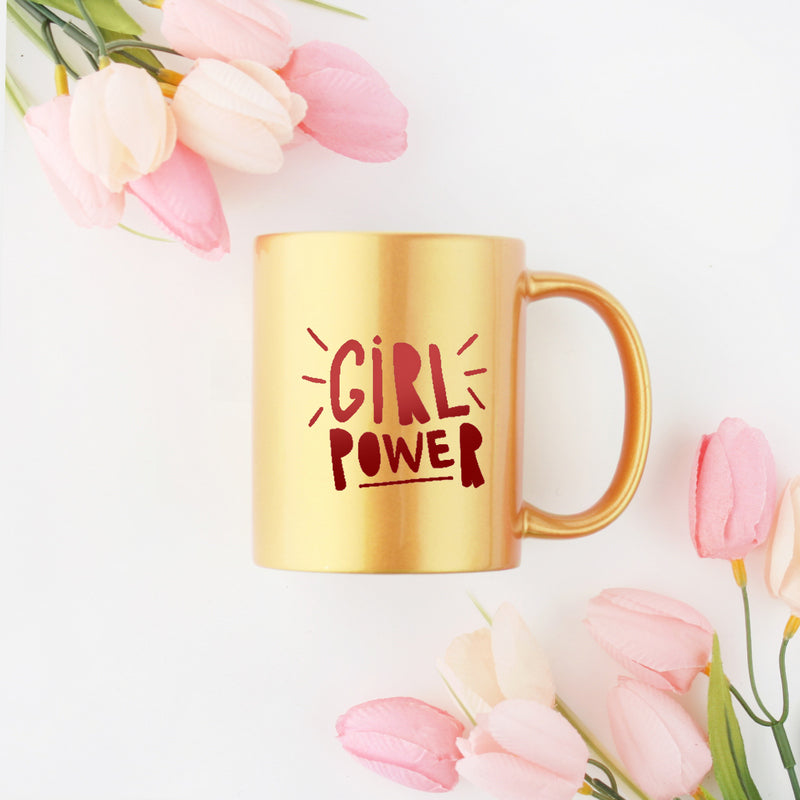A stylish ceramic mug featuring hand-lettered typography celebrating girl power, adorned with gold and silver accents.