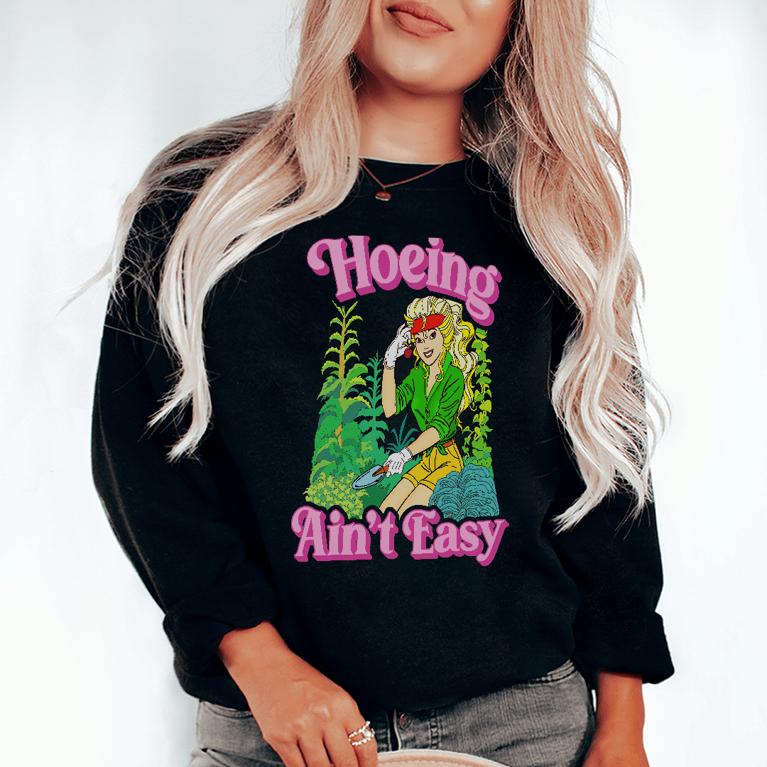 A cozy 'Hoeing Ain't Easy' hoodie featuring a cotton/poly fleece blend, perfect for warmth and style.