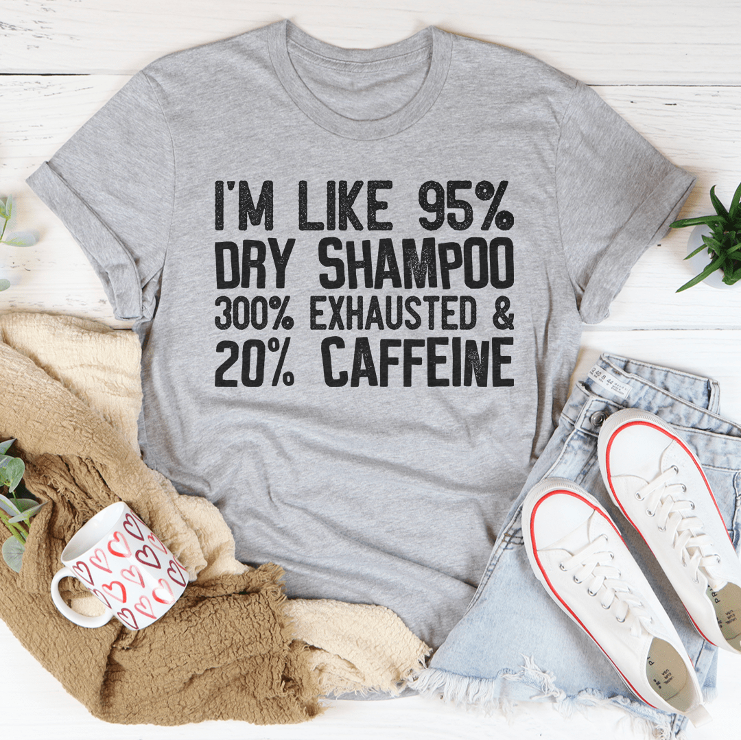 A stylish t-shirt featuring the phrase 'I'm Like 95% Dry Shampoo 300% Exhausted And 20% Caffeine' printed on soft cotton fabric.