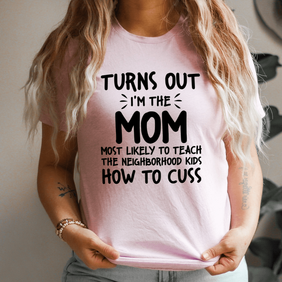 A humorous t-shirt featuring the phrase 'I'm The Mom Most Likely To Teach The Neighborhood Kids How To Cuss', made from soft cotton.