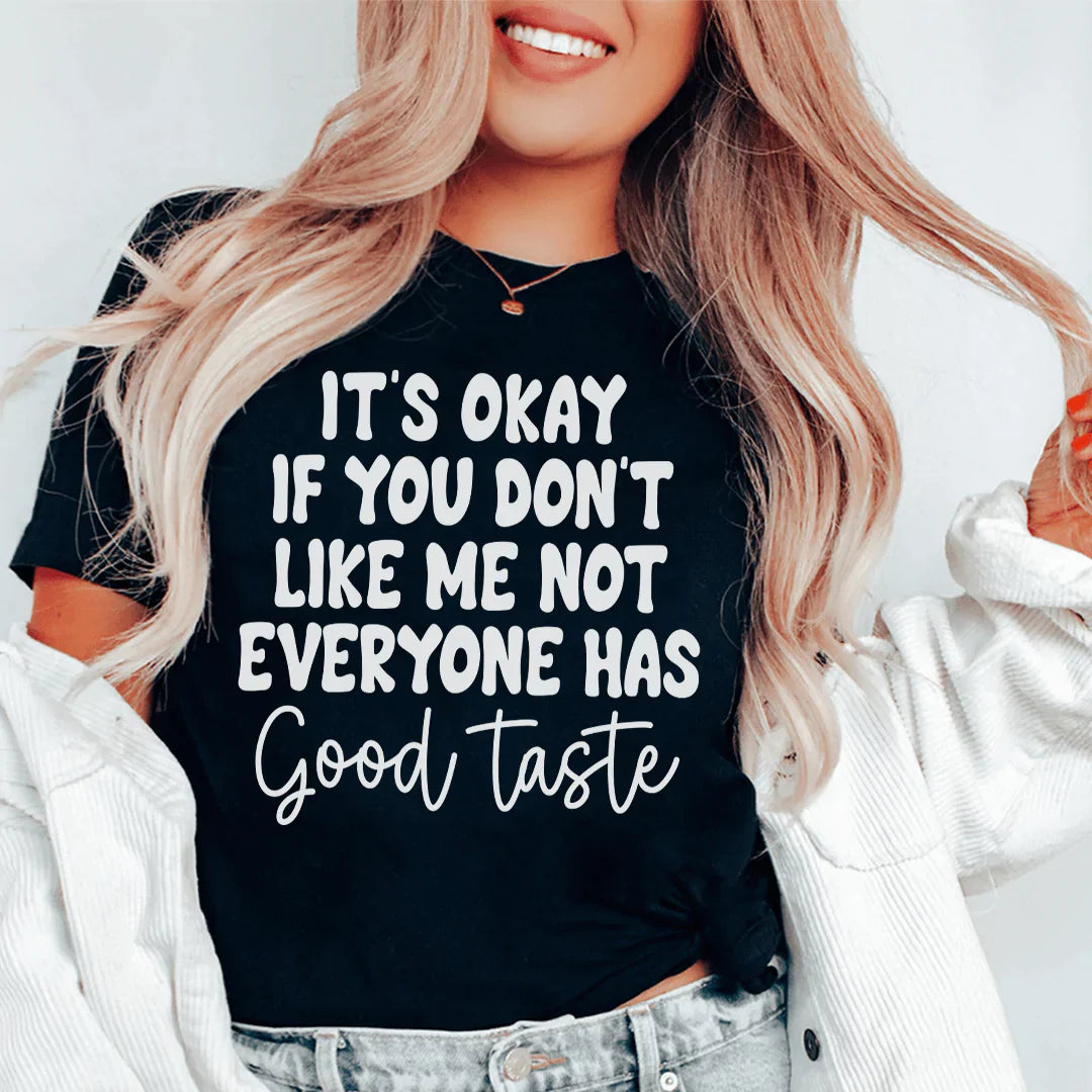 A stylish black t-shirt featuring the phrase 'It's Okay If You Don't Like Me Not Everyone Has Good Taste' printed in bold letters.