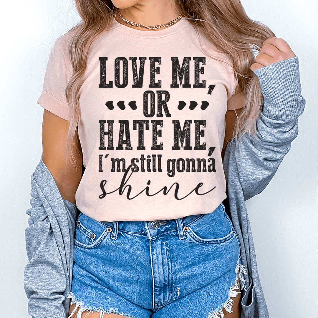 A stylish black t-shirt with the phrase 'Love Me Or Hate Me I'm Still Gonna Shine' printed on the front, showcasing its soft fabric and durable stitching.