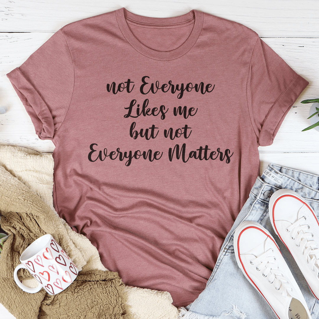 Not Everyone Likes Me But Not Everyone Matters T-Shirt displayed on a hanger, showcasing its soft cotton fabric and bold print.