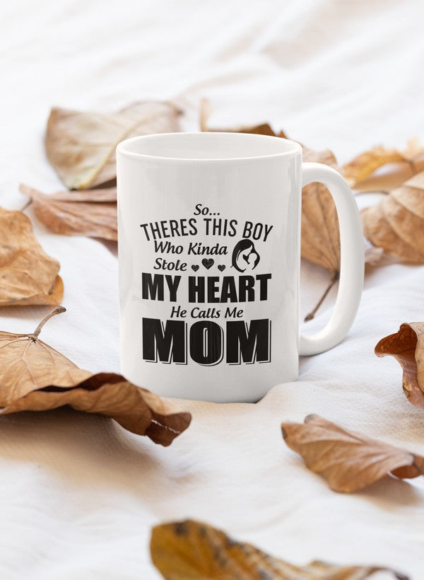 A charming 11oz ceramic mug with a glossy finish, featuring the phrase 'So There's This Boy Who Kinda Stole My Heart He Calls Me Mom' in stylish typography.