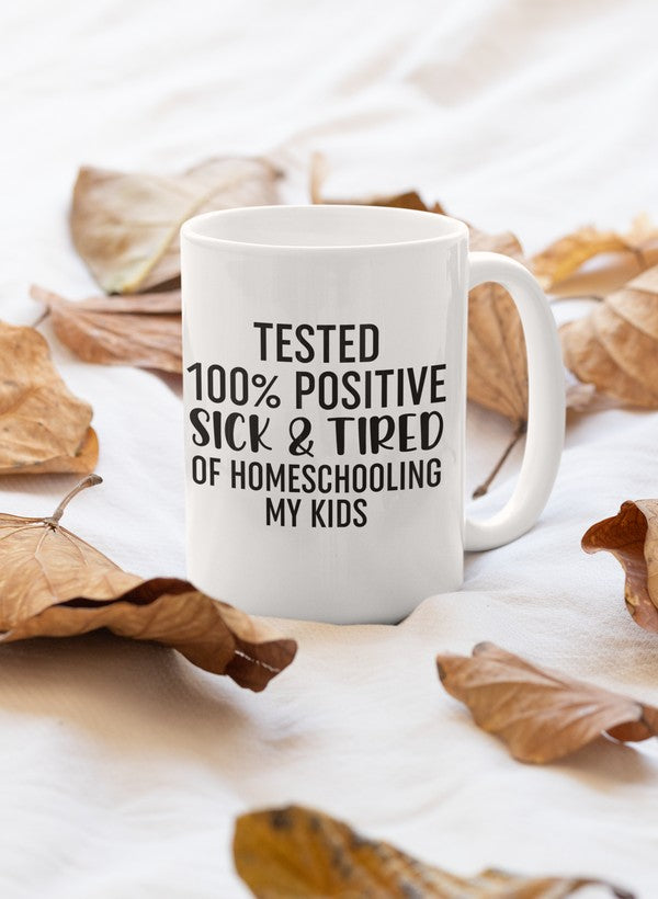 A glossy 11oz ceramic mug with a humorous design that reads 'Tested 100% Positive Sick & Tired Of Homeschooling My Kids', featuring a sturdy handle.