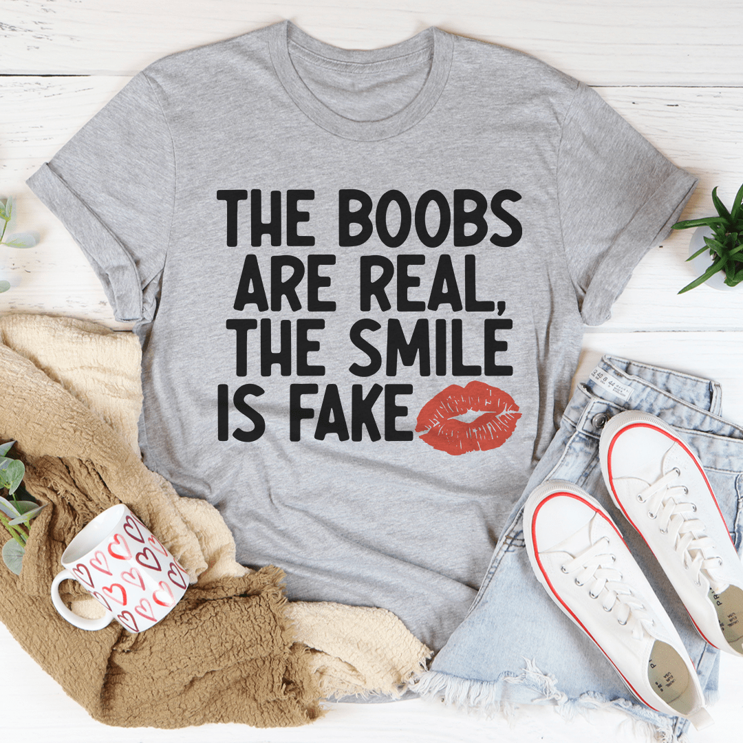 A stylish t-shirt featuring the slogan 'The Boobs Are Real The Smile Is Fake', made from soft cotton with double stitching.