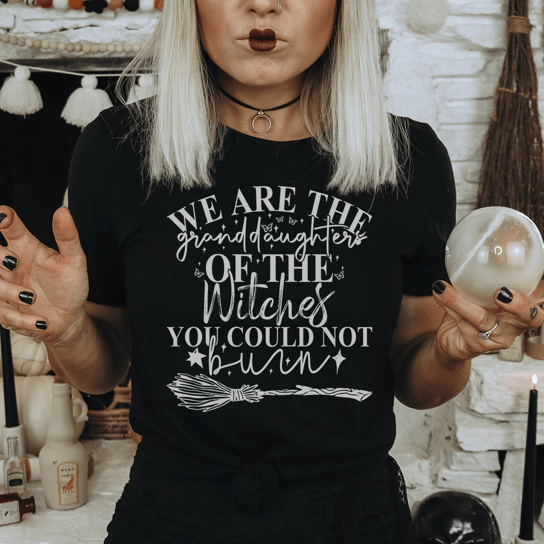 A stylish black t-shirt featuring the phrase 'We Are The Granddaughters Of The Witches You Could Not Burn' in bold white lettering.