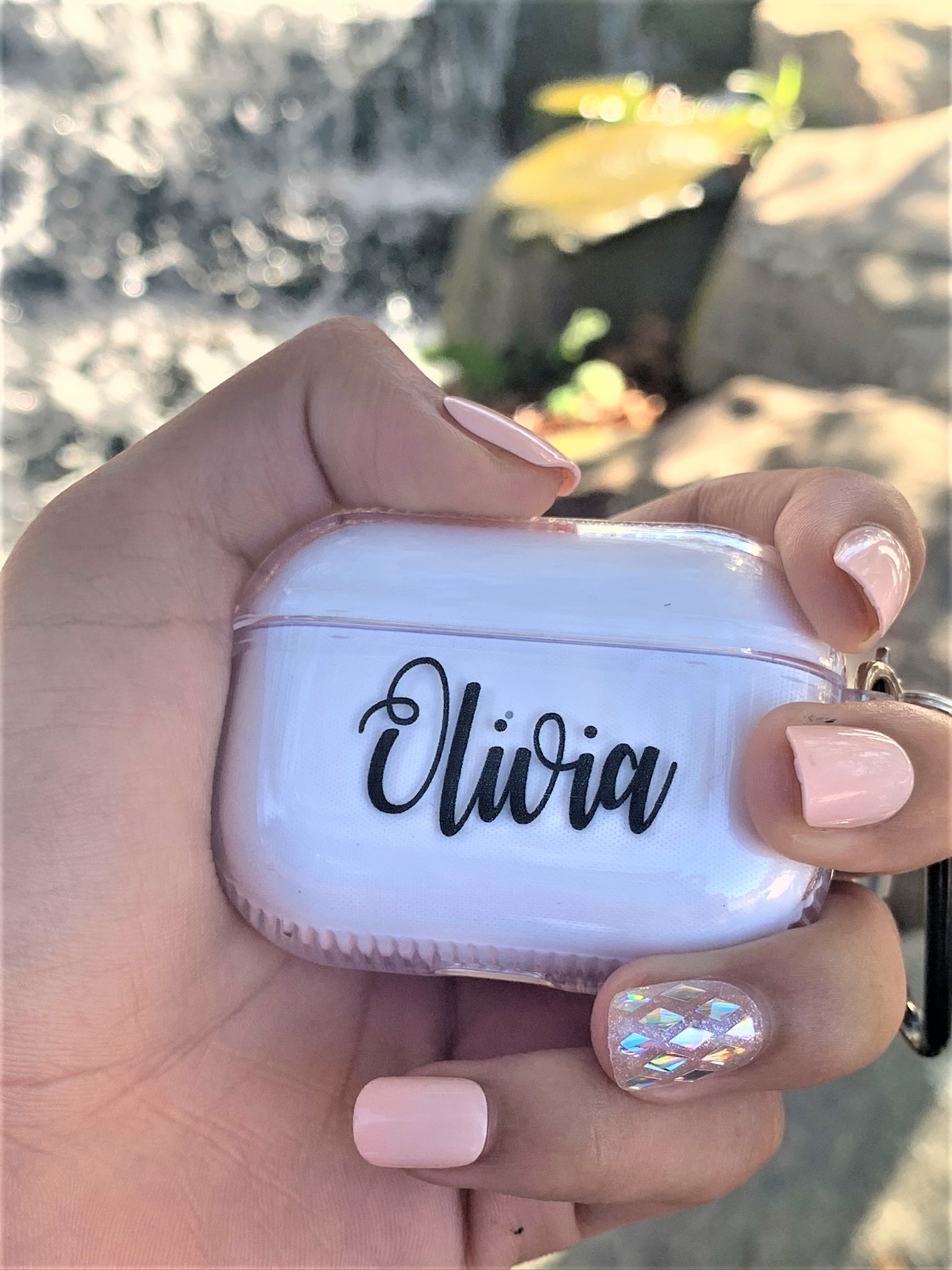 A personalized transparent case for Apple AirPods Pro, showcasing a sleek design with a metal strap attached.