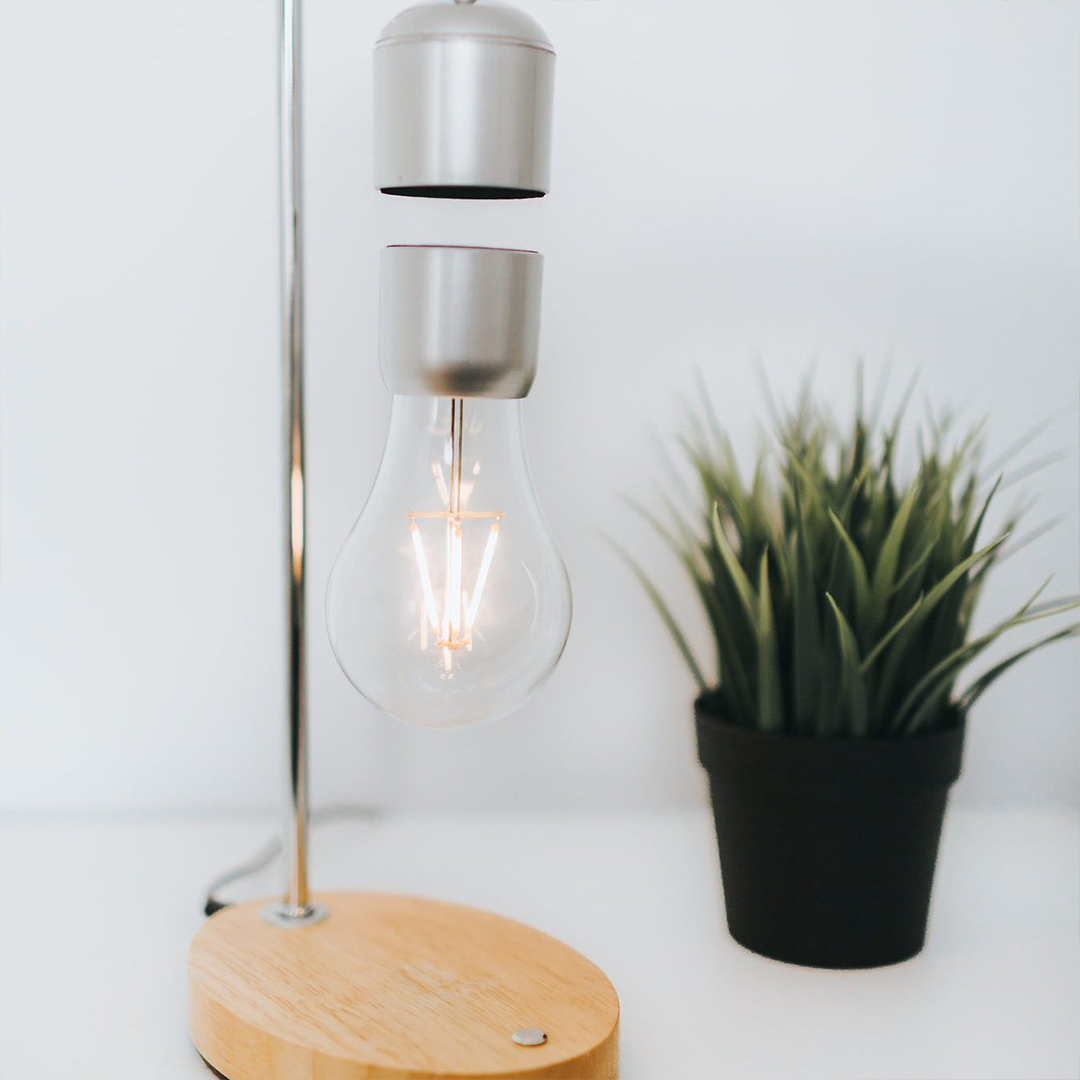 A modern levitating wireless light bulb lamp with a wooden oak finish base and a floating light bulb, showcasing innovative design and technology.