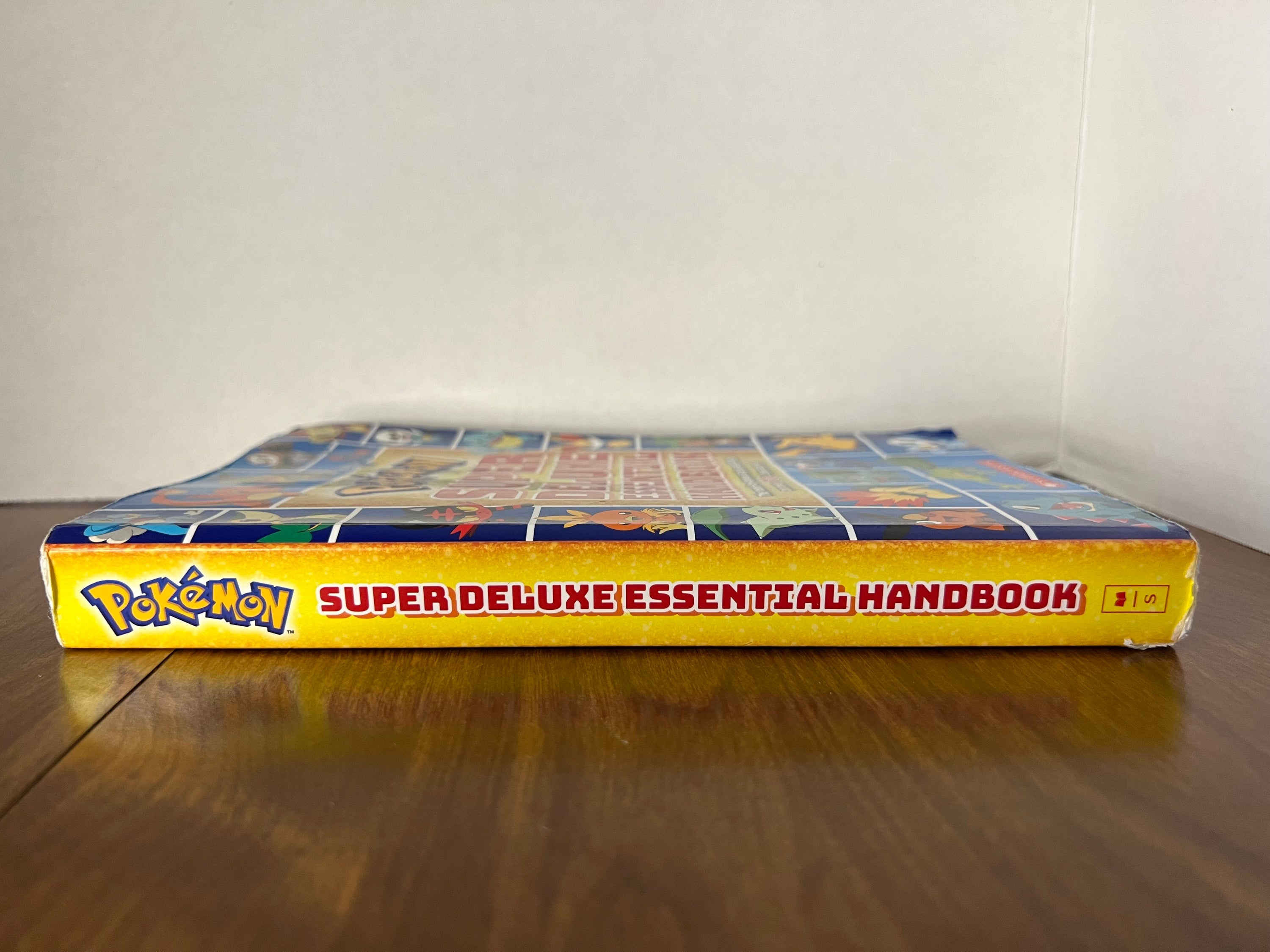 Cover of the Pokémon Super Deluxe Essential Handbook featuring colorful illustrations of various Pokémon characters.