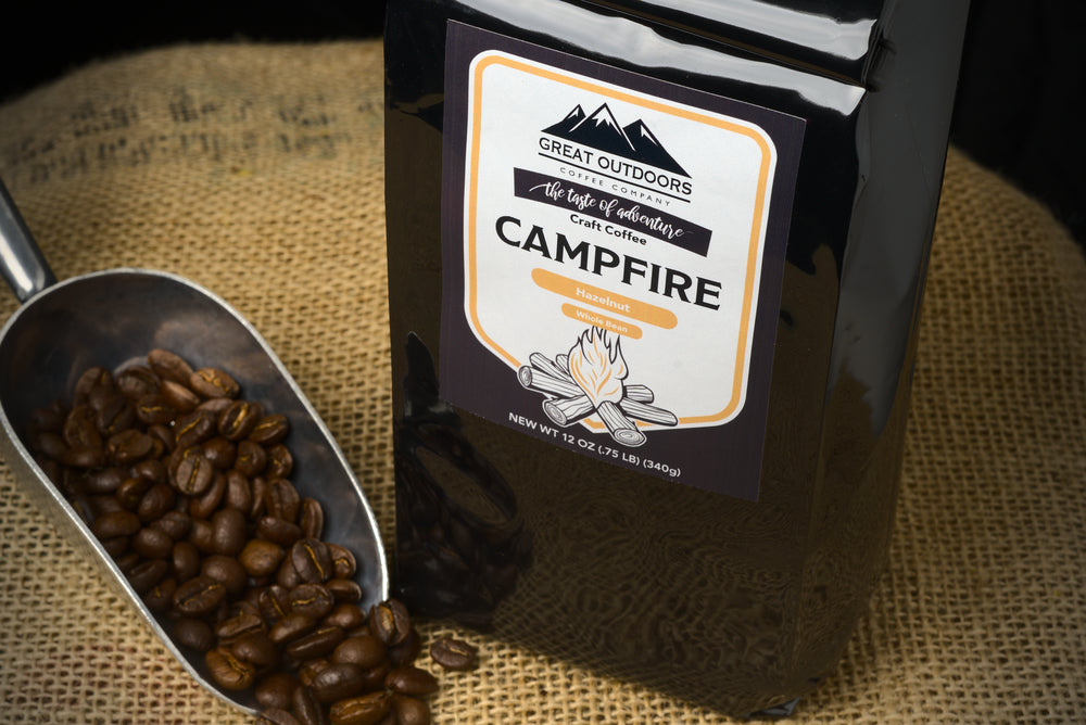 A steaming cup of Campfire Craft Coffee with hazelnut flavor, surrounded by nature, evoking a cozy campfire atmosphere.