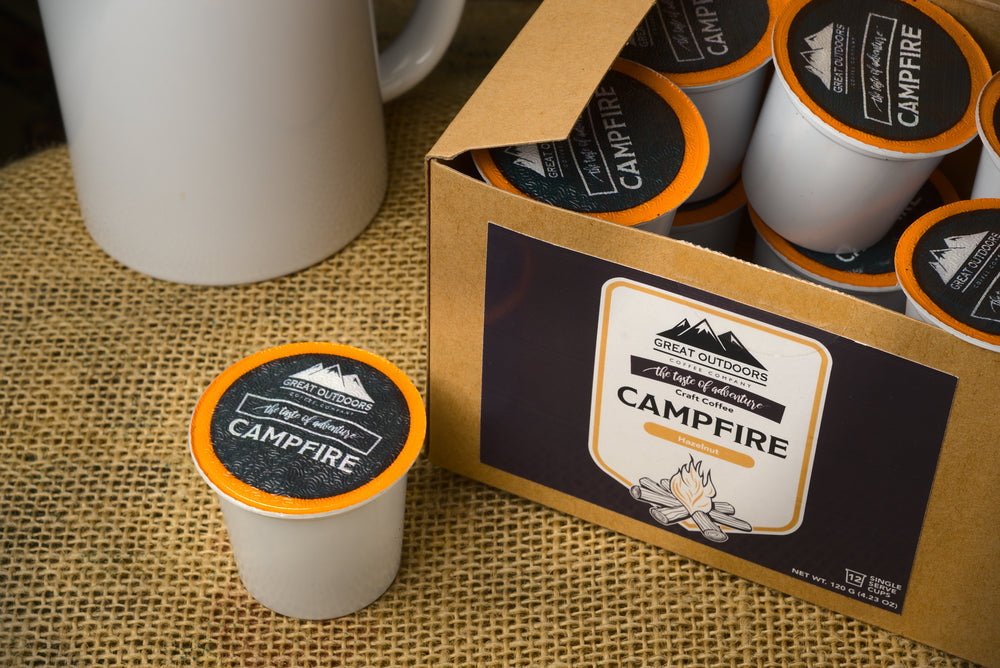 A steaming cup of Campfire Craft Coffee with hazelnut flavor, surrounded by nature, evoking a cozy campfire atmosphere.