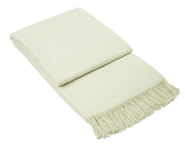 Chiswick Throw blanket in ivory, made from luxurious merino wool and cashmere, elegantly draped on a sofa.