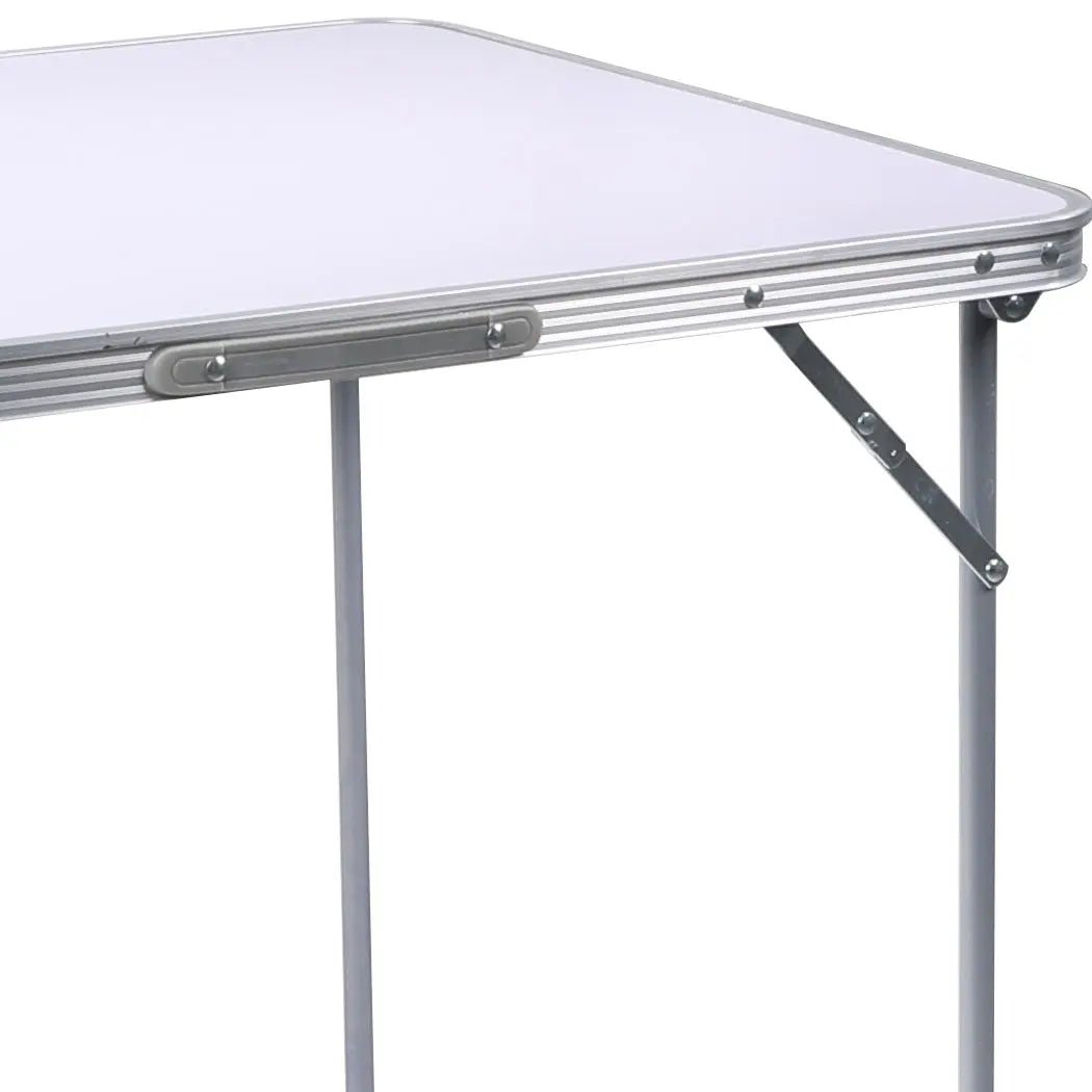 A lightweight and portable folding camping table made of aluminum, set up outdoors with a scenic background, perfect for picnics and camping.