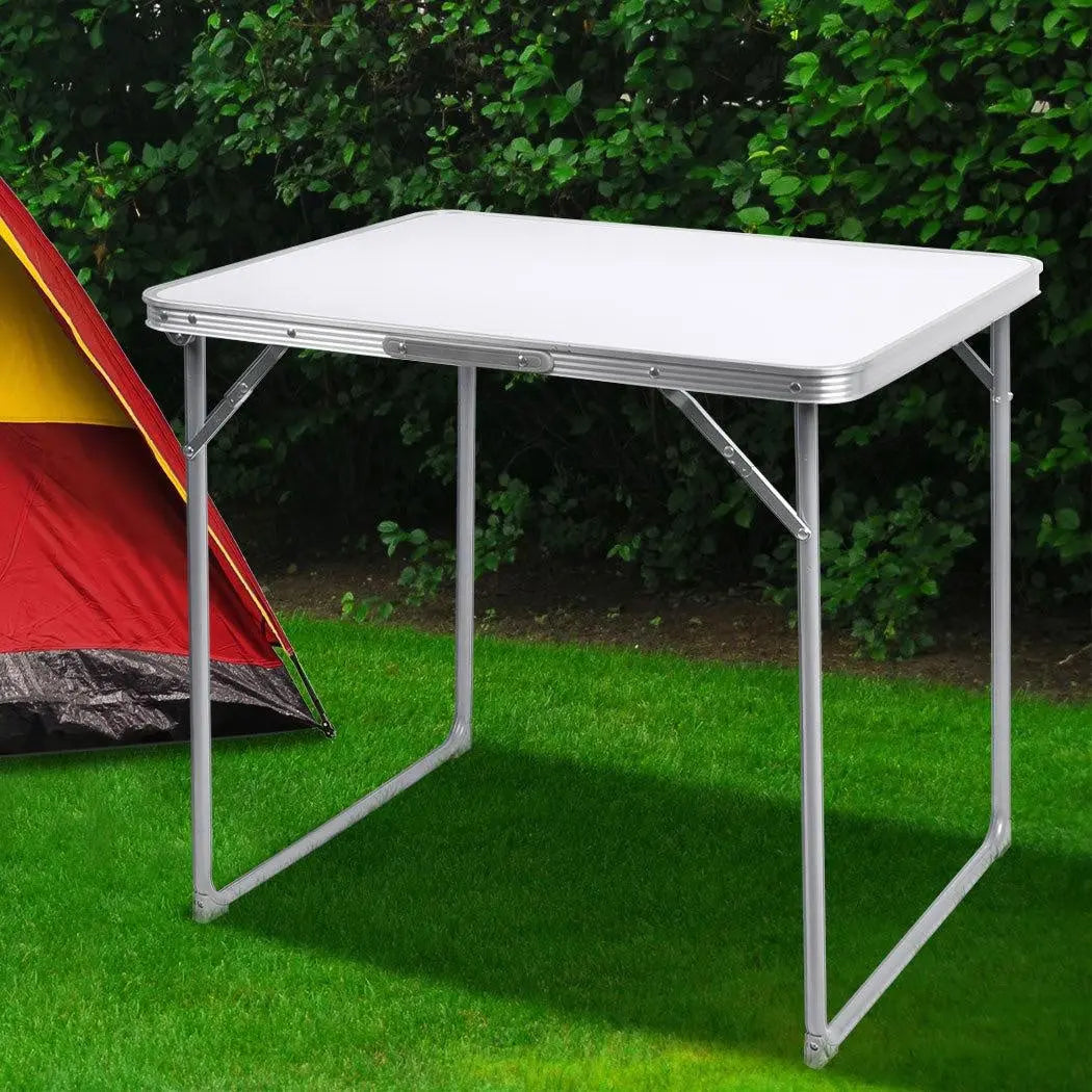 A lightweight and portable folding camping table made of aluminum, set up outdoors with a scenic background, perfect for picnics and camping.