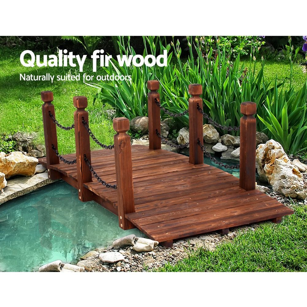 A rustic wooden garden bridge made of burnt fir wood, featuring an arch design and rustic chains along the railings, set in a lush garden landscape.