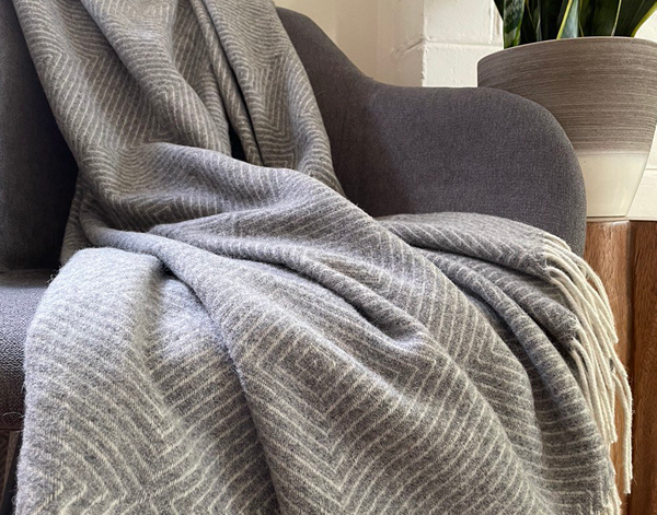 Hampton Throw blanket in light grey, made from Merino wool blend, elegantly draped over a sofa, showcasing its soft texture and luxurious design.