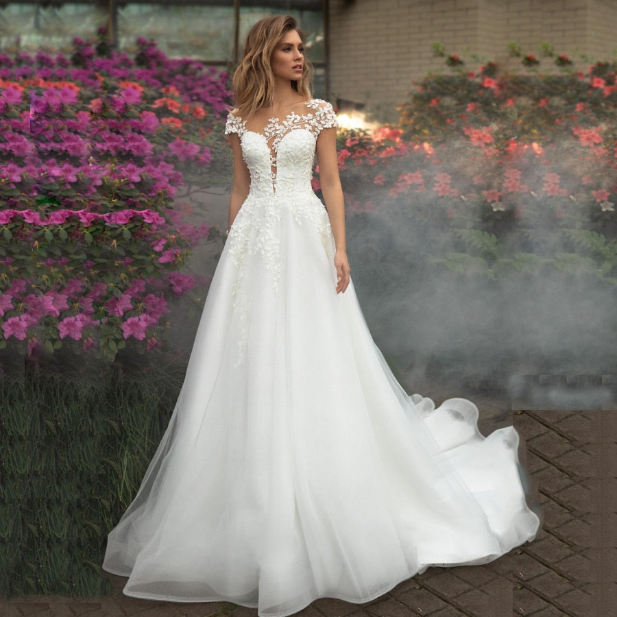 Elegant Wedding Dresses Vertigo De Novia featuring short sleeves, scoop neck illusion, and flower appliqué details in tulle fabric.